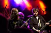 To musikere spiller gitar på en scene med rødt og lilla lys og mikrofonstativer i bakgrunnen.