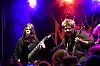 To musikere opptrer på en opplyst scene foran publikum med røyk og rødt scenebakteppe.