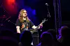 En gitarist opptrer på en mørk scene foran publikum, med blått og lilla lys.