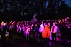 Et stort publikum står tett samlet utendørs i mørket mens scenelys lyser opp området.