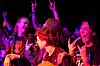 Tre publikummere foran scenen smiler, synger og gjør rockehend-tegn i rosa lys.