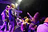 Et rockeband spiller på en utendørsscene foran et tett publikum som strekker armene i været.