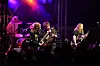 Et rockeband spiller på en utendørs scene med trommesett, gitarer og lilla scenelys.