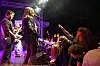 Et rockeband spiller på en opplyst scene mens publikum står tett foran og rekker hendene i været.
