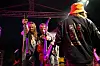 Tre musikere på en mørk scene med gitarer og mikrofon, sett bakfra mot publikum.
