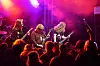 Tett publikum foran en scene med tre musikere og sterke lilla og røde lys.