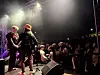 To musikere står på en scene foran et publikum i mørket, med scenelys og røykeffekt.