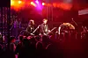 Et rockeband spiller på en scene foran et tett publikum under rødt og lilla scenelys.