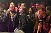 Et tett publikum i svart klær står foran en scene og reagerer entusiastisk under en rockekonsert.
