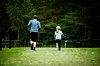To personer sett bakfra jogger på en grønn gresslette med trær i bakgrunnen.