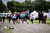 En gruppe løpere konkurrerer på en grusvei med publikum, telt og trær i bakgrunnen.
