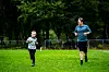 To personer jogger på en grønn gresslette med trær i bakgrunnen.