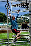 En mann henger med strake armer i gymnastikkringer ved et utendørs hinder med metallramme.