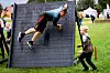 To personer deltar i et hinderløp med en høy vegg på en gressbane.