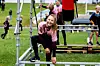 Et barn sitter og smiler på en metallkonstruksjon i en utendørs leke- og hinderløype.