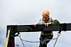 Et barn med lysekrøllet hår klatrer over en mørk bjelke på en lekeplass.