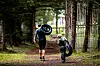 To personer går med sykler på en skogssti omgitt av trær og gjerder.