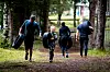 Fire personer går på en sti i skogen, to av dem bærer store dekk under trening.