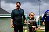 En mann og et barn står på en fotballbane med grønne mål og flere fotballer i bakgrunnen.