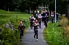En gruppe løpere beveger seg opp en grussti mellom trær og gress i et skogsområde.