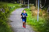 En person i blå løpeklær løper på en grusvei omgitt av gress og trær.