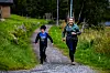 To personer jogger på en grussti mellom gress og trær i et utendørs grøntområde.