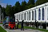 Arbeidere og en rød gaffeltruck foran en lang, hvit arrangementshall i grønne omgivelser.