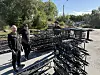 To personer ved svarte metallkonstruksjoner på et asfaltert uteområde med trær i bakgrunnen.