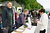 Flere personer møtes ved et utleveringsbord mellom varebiler på en utendørs markedsplass.