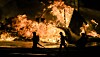 Store flammer lyser opp natten bak silhuetter av mennesker.