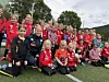 En stor gruppe unge fotballspillere poserer sammen på en kunstgressbane.