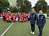 En stor gruppe unge fotballspillere og trenere poserer på en kunstgressbane.