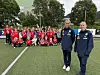 En stor gruppe unge fotballspillere og trenere poserer på en kunstgressbane.