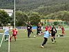 Unge jenter spiller fotball på en kunstgressbane mens trenere følger treningen.