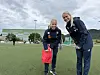 To kvinner i fotballklær står på en kunstgressbane under en overskyet himmel.