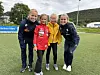 To voksne og to barn står sammen på en fotballbane og smiler mot kameraet.