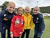 To voksne i mørkt treningstøy og to jenter poserer på en fotballbane.