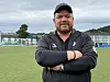 Skjegget mann i svart treningsjakke står med korslagte armer på en fotballbane.