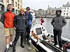 Fire menn står ved siden av en hvit robåt på en brygge i en byhavn.