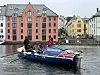 Blå og rød båt med flere personer på en kanal foran fargerike bygninger.