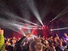 Konsertpublikum med løftede armer foran en scene med røde og hvite lyskastere.