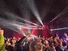Konsertpublikum med løftede armer foran en scene med røde og hvite lyskastere.