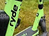 Nærbilde av grønne Ryde-elsparkesykler med svarte detaljer på vått gress.