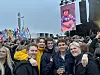 En tett folkemengde foran en festivalscene, med en gruppe unge personer i forgrunnen og fargerike flagg bak.