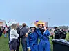 To personer i blå regnponchoer poserer foran en festivalplass med pariserhjul og publikum.