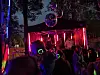 Publikum ser en artist opptre på en liten scene med rødt lys og discokuler i mørket.