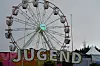 Et stort pariserhjul står bak Jugend-skiltet ved et festivalområde med telt og trær.