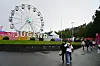 Festivalgjengere går over en våt plass foran Jugend-skiltet og et stort pariserhjul.