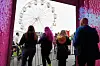 Festivalgjester står ved et gjerde foran et opplyst pariserhjul, omgitt av fargerike LED-skjermer.