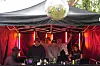 Flere personer står ved et DJ- og scenebord under rødt lys, med en discokule over scenen.